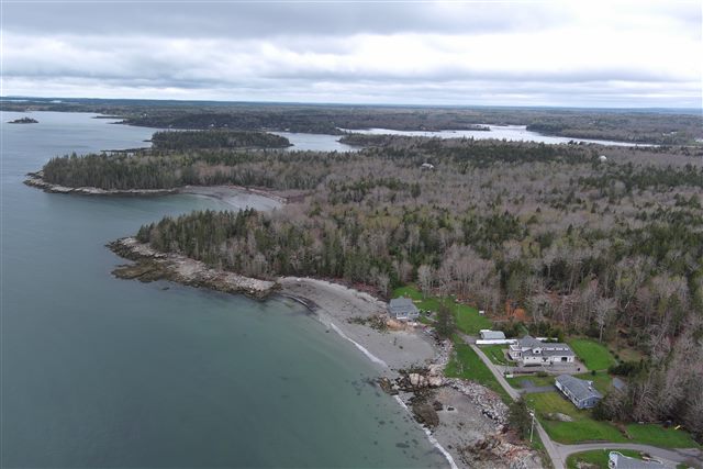 Aerial view along a wooded coast with coves, scattered homes, and offshore islands