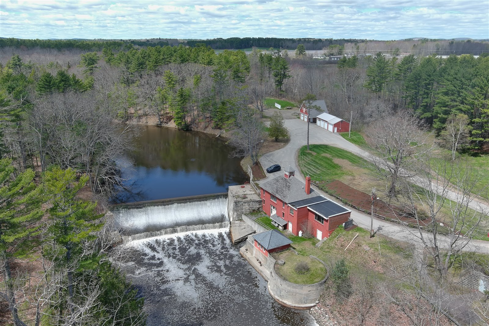 Aerial view of a dam, river, roads, buildings, and surrounding woodland